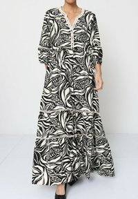 Robe maxi en imprimé floral noir et blanc, avec un décolleté en V, des manches trois quarts et un tissu texturé à volants.