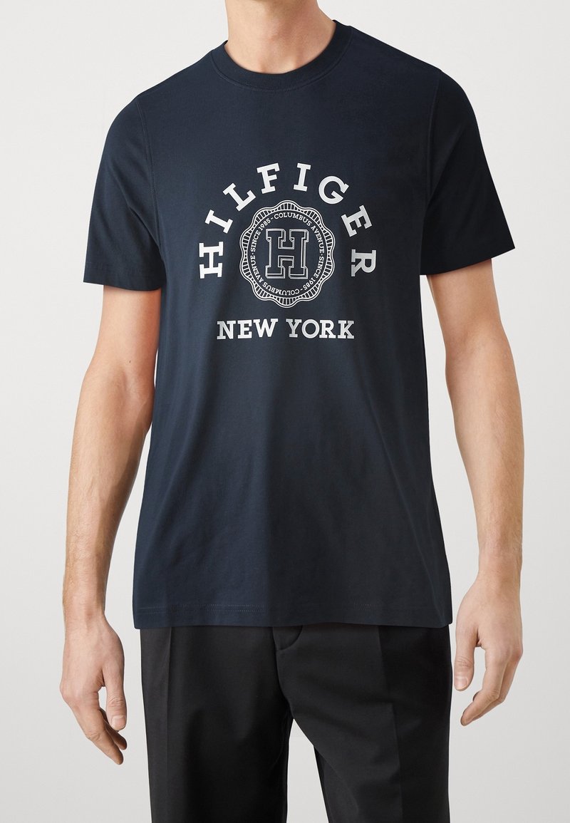 Námornická bavlněná tričko s kulatým výstřihem, s bílým kruhovým logem a nápisem "HILFIGER NEW YORK" tučným písmem, umístěným centrálně na hrudi.