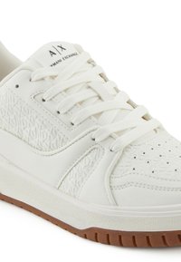 Sneaker bianca bassa con pannelli laterali testurizzati, lacci bianchi, punta traforata e suola in gomma marrone, con marchio Armani Exchange sulla linguetta.