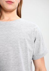 Grå kortærmet t-shirt lavet af let, blødt stof. Har en rund halsudskæring og opsmøgede ærmer, med en glat, meleret tekstur.