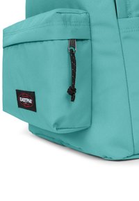 Zaino turchese con tasca frontale e zip nera, caratterizzato da un tessuto testurizzato e un logo Eastpak rosso e nero.