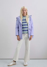 Chaqueta impermeable de color púrpura claro con capucha, con broches negros, combinada con un suéter a rayas azul y verde y pantalones acampanados blancos. Zapatillas blancas.