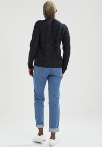Schwarzer Strickpullover mit strukturiertem Muster, taillierten Bündchen und rundem Ausschnitt, kombiniert mit hellblauen Jeans mit umgeschlagenem Saum und weißen Sneakers.