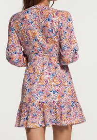 Vestido de manga corta con un vibrante estampado de paisley en naranja, rosa y azul sobre un fondo claro, con un dobladillo con volantes y cintura elástica.