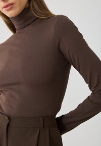 Barna, hosszú ujjú, garbós felső, puha anyagból készült, testhezálló fazonnal és sima textúrával, melyet magas derekú nadrággal párosítanak.
