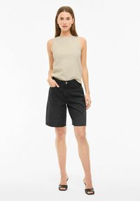 Top sin mangas de textura beige combinado con shorts de mezclilla negros, con un corte relajado y dobladillo sin rematar. Llevado con sandalias negras de punta abierta.