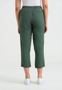Gröna linnebyxor i cropped-modell med mjuk textur, elastisk midja och uppvikta fållar, med två bakfickor och en avslappnad passform.