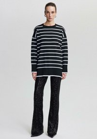 Svartvitt randig oversized tröja med rund hals, kombinerad med svarta paljettbyxor med utsvängd ben. Inkluderar blanka detaljer och en slät textur.