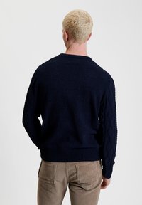 Maglione lavorato a maglia blu navy con motivo a trecce testurizzato sulle maniche e orlo a costine. Tessuto morbido; scollatura rotonda, silhouette aderente.