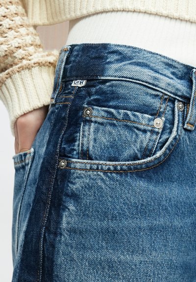 Blugi din denim albastru deschis, cu buzunar frontal, accesorii argintii și panouri contrastante din denim mai închis la culoare. Textură moale cu detalii de cusături vizibile.