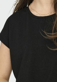 Top nero a maniche corte con un delicato motivo testurizzato. Presenta un collo rotondo ed è abbinato a una sottile collana d'oro con perle.