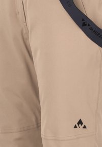 Pantaloni corti beige realizzati in tessuto leggero, con un logo nero sull'orlo e una vita blu navy con marchio. Texture liscia, senza motivi.