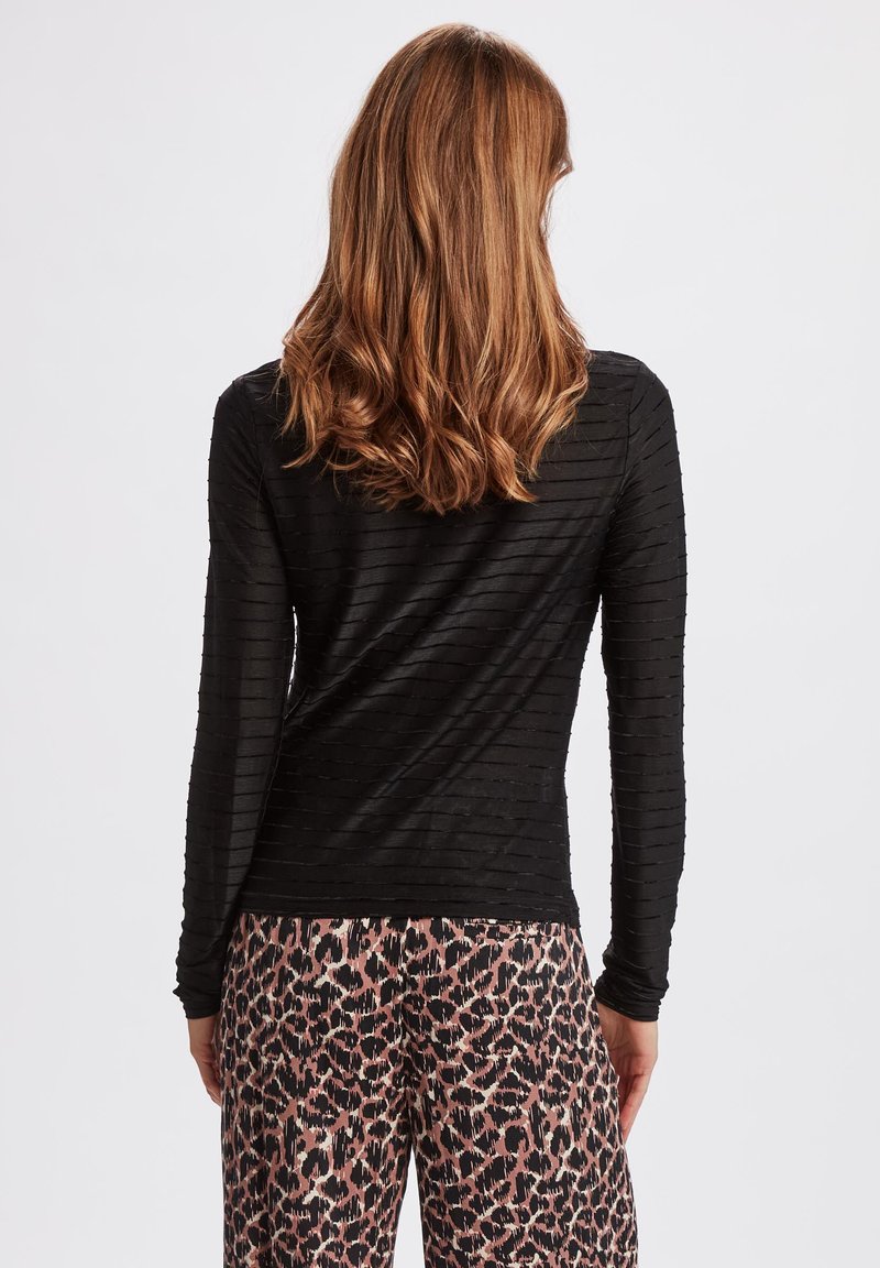 Schwarzes Langarmoberteil mit strukturierten Streifen, kombiniert mit rosa und schwarzen Leopardenmuster-Hosen. Der Fokus liegt auf unterschiedlichen Textilmustern und Farbkontrasten.