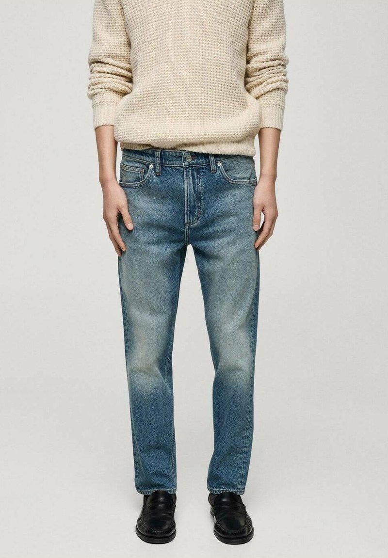 Jeans in denim azzurro chiaro con vestibilità rilassata, finitura sbiadita, cinque tasche e passanti per cintura, abbinati a un maglione a trama crema.