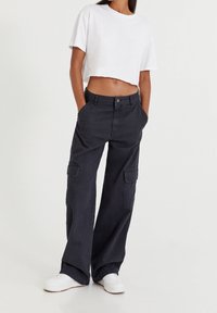 Lyhyeksi leikattu valkoinen t-paita yhdistettynä tummanharmaisiin, leveälahkeisiin cargo-housuihin, joissa on sivutaskut ja nappisuljenta, sekä valkoiset tennarit.