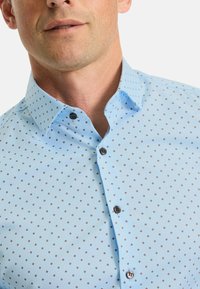 Light blue shirt with a small geometric pattern in dark red and white. Features a collar, button-down front, and textured fabric.