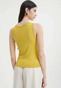Ärmelloses gelbes Strickoberteil mit geripptem Saum und Ausschnitt. Weicher Stoff, figurbetonendes Design und minimale Rückendetails.