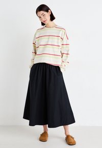 Stripet, lett kremfarget genser med grønne, rosa og røde linjer, sammen med et knelengde, svart samlet skjørt og brune slip-on sko.