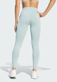 Lichtgroene, hooggesneden legging van rekbaar materiaal, met een gladde textuur en gestroomlijnd ontwerp, gecombineerd met witte sneakers.