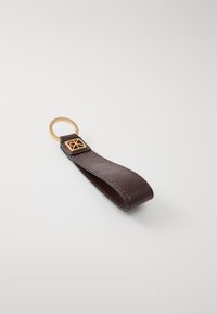 Porte-clés en cuir marron avec une surface texturée, comportant un anneau en métal doré et un emblème doré sur un onglet rectangulaire.