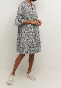 Robe abstraite noire et blanche avec un col et des manches cloche, dotée d'une coupe ample et d'un ourlet au niveau des genoux. Associée à des baskets légères.