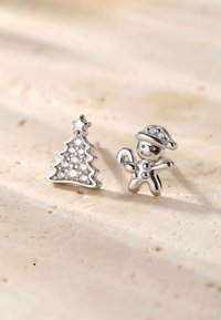 Silver earrings featuring a Christmas tree and a gingerbread man, embellished with clear stones, set against a light textured background.