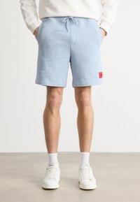 Șorturi de trening bleu deschis, cu talie elastică și șnur, având bochete laterale și un patch roșu al mărcii pe coapsa stângă.