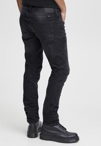 Zwarte denim jeans met een slim fit, voorzien van achterzakken en een gladde textuur. Gecombineerd met zwarte veterschoenen.