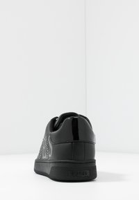 Zwarte sneaker van glanzend gepatenteerd leer met textuurdetails. Voorzien van zilveren versieringen en een rubberen zool met textuur. Merken op de achterkant.