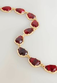 Złota naszyjnik z dużymi, oszlifowanymi czerwonymi kamieniami w kształcie łez, połączonymi małymi ogniwami. Gładkie wykończenie z błyszczącymi powierzchniami.