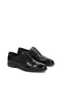 Zapatos de vestir de cuero negro con un acabado suave, diseño de puntera cap, y cinco ojales para cordones; cuentan con un tacón bajo y apilado.