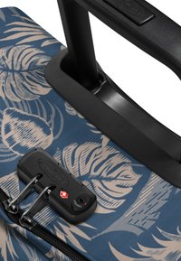 Maleta con ruedas con tela azul que presenta patrones botánicos en color crema, un asa negra y una cerradura aprobada por la TSA cerca de la cremallera.