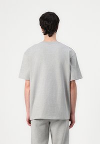 Tricou gri cu mânecă scurtă dintr-un amestec moale de bumbac, având un croi lejer și guler rotund, prezentat din spate. Textură netedă.