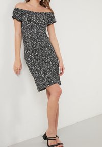 Sort off-shoulder kjole med hvidt blomstermønster, tætsiddende design, korte ærmer og knælang. Glat stof og flaret kant.
