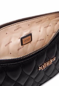 Borsa a tracolla nera trapuntata con logo dorato sul lato esterno, caratterizzata da un interno beige con motivo ripetuto del logo del marchio e chiusura con zip.