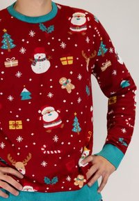 Red sweater with a variety of Christmas-themed patterns, including Santa, snowman, Christmas trees, and gifts. Finished with turquoise cuffs.