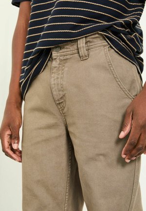 Beige cotton trousers with a straight cut. Features front pockets and a belt loop, paired with a navy striped shirt. Smooth texture.