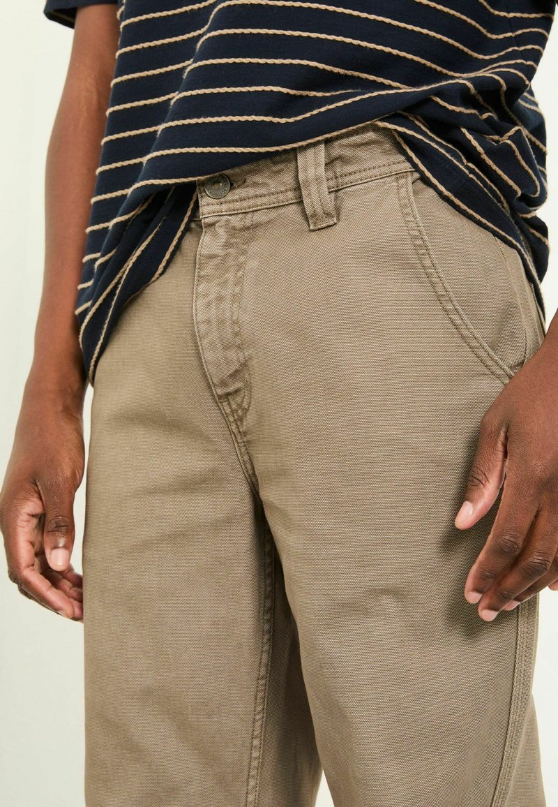 Beige cotton trousers with a straight cut. Features front pockets and a belt loop, paired with a navy striped shirt. Smooth texture.