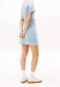 Světle modré pruhované denimové šaty s krátkými rukávy, detailem pásku v pase a rozšířeným lemem, doplněné bílými teniskami a ponožkami.