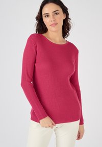 Pull côtelé à manches longues en fuchsia, présentant un col rond et un tissu texturé. Associé à un pantalon de couleur claire.