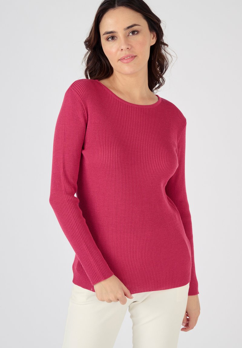 Pull côtelé à manches longues en fuchsia, présentant un col rond et un tissu texturé. Associé à un pantalon de couleur claire.