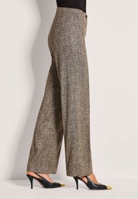 Bruine herringbone wijde broek met hoge taille, gemaakt van textuurstof. Draagt bij zwarte slingback hakken met gele accenten.