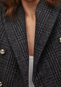 Dvouřadový černobílý blazer se vzorem v šedých tónech a metalickými knoflíky, který má strukturovanou látku a široký klopový design.