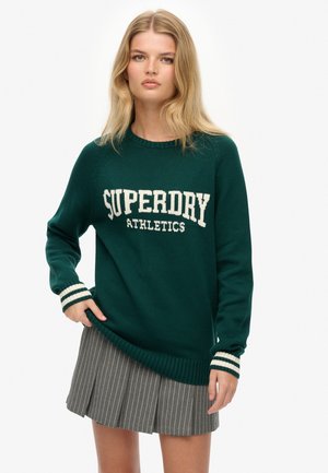 Ciemnozielony dzianinowy sweter z białym logo "SUPERDRY ATHLETICS", prążkowanymi mankietami w paski i luźnym krojem. W połączeniu z spódnicą w prążki.