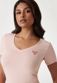 Lyserød V-hals T-shirt lavet af blød bomuld. Har et lille rødt trekantet logo på venstre brystområde. Korte ærmer.