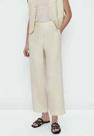 Woman wearing beige wide-leg pants, a matching vest, beige top, and black flat sandals with double buckle straps.