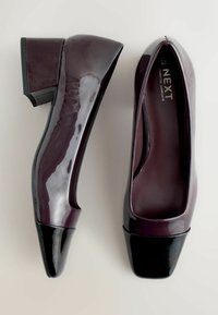 Burgundia lakknahast kontsad musta ruudukujulise ninaga ja paksu kandiga. Sile viimistlus kerge läikega. Ümar disain taga.