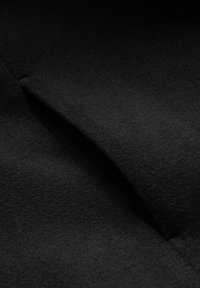 Tejido negro texturizado con un acabado suave. La superficie muestra un ligero brillo y suaves pliegues, lo que enfatiza la profundidad y calidez.
