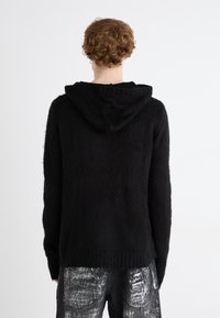 Sweater preto, texturizado, com capuz e um corte largo, apresentando um acabamento ribado nas bainhas e punhos. Material suave, adequado para uso casual.