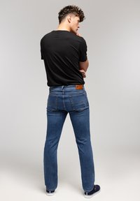 Męskie niebieskie dżinsy z prostymi nogawkami, z jasnym praniem, kontrastowymi szwami i brązową skórzaną łatą na pasku.